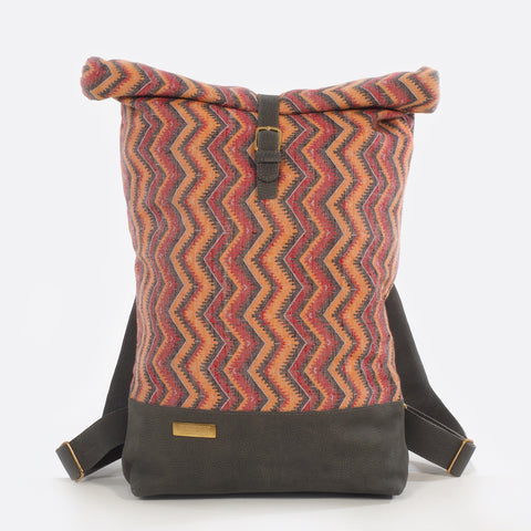Front view of backpack with handwoven traditional dhaka fabric from Nepal and leather.  The fabric  of the backpack is mainly red, orange and black and the leather is grey . The bag has brass buckles