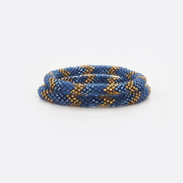 Set of two beaded bracelets.  The bracelets are made from mat blue, shiny blue and shiny golden glass beads. The bracelets have the same geometric pattern. The Battiayo bracelets are handmade from small glass beads. The glass beads are clearly shown. The background of the picture is white.