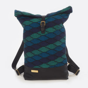 Front view of Battiayo ,Deep Blue Sea' backpack with handwoven traditional dhaka fabric from Nepal and leather. The handwoven fabric of the backpack has three different shades of blue and a bit of black. The dhaka fabric has a geometric pattern and is handwoven by amazing women. The leather is black. The straps and bottom are made from leather. The brass buckles and brass label are also made in Nepal.