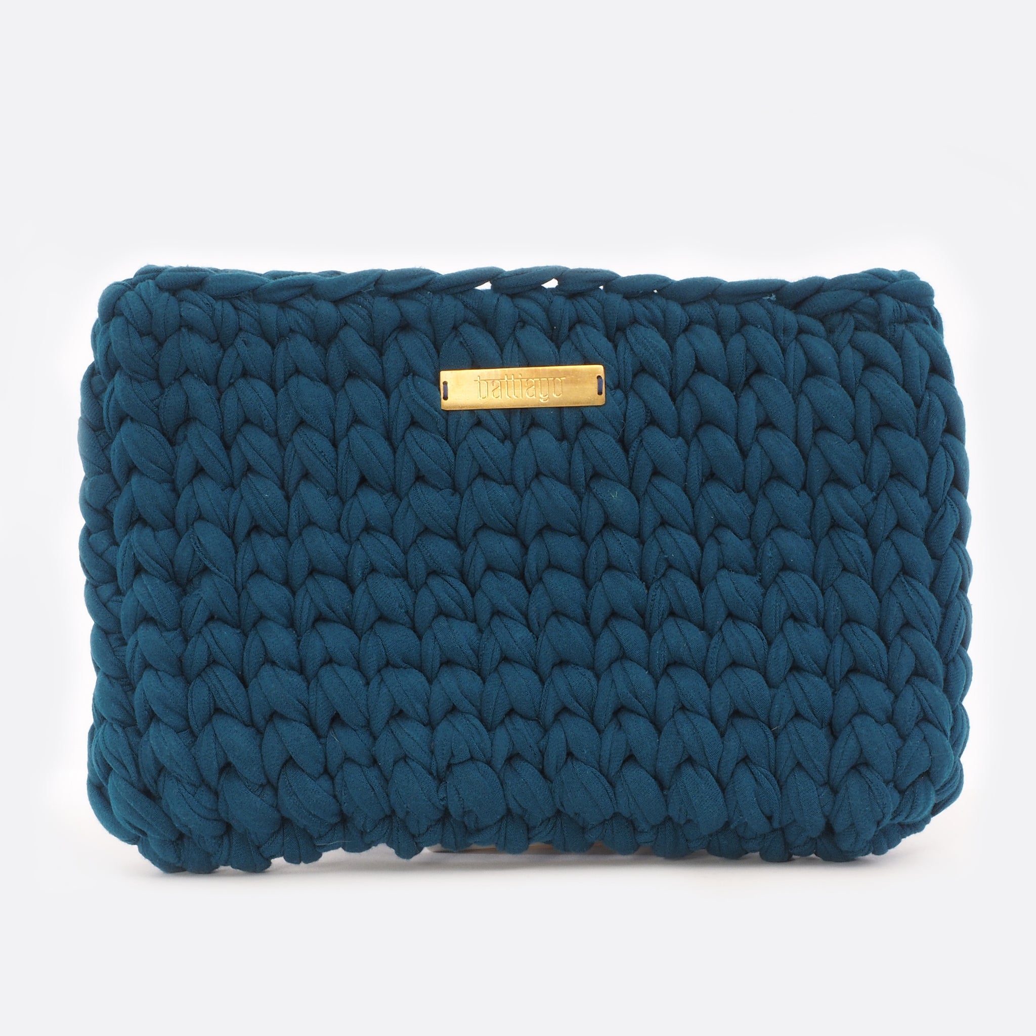Front view of the big dark blue Battiayo clutch. The bag is crocheted by women. The handcut brass label is placed in the middle of the bag, close to the top. The bag is a chunky crocheted clutch. 