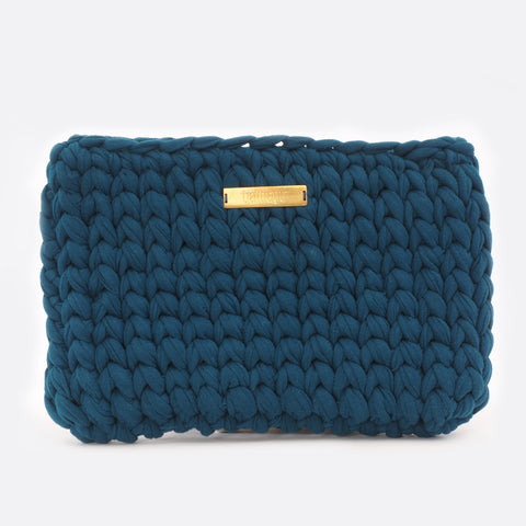 Front view of the big dark blue Battiayo clutch. The bag is crocheted by women. The handcut brass label is placed in the middle of the bag, close to the top. The bag is a chunky crocheted clutch. 