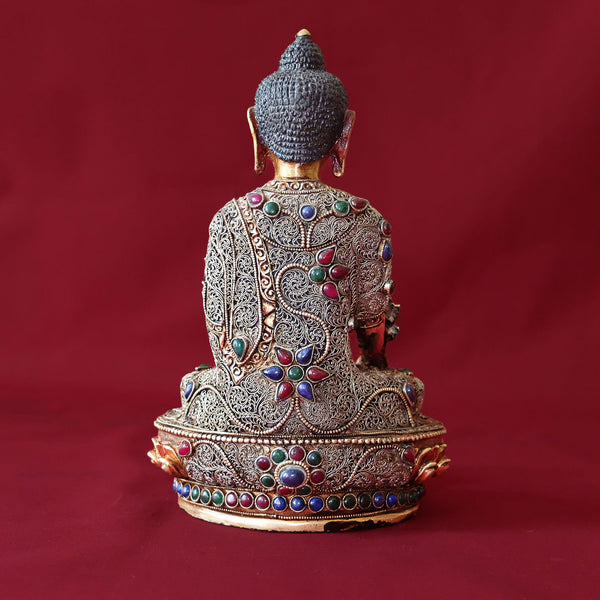 Bhaisajyaguru Statue made of copper, lost wax casting, silver and gold plated, set with filigree and set synthetic gemstones in ruby red, emerald green, lapis lazuli blue. The face is set in gold. Handmade in Nepal