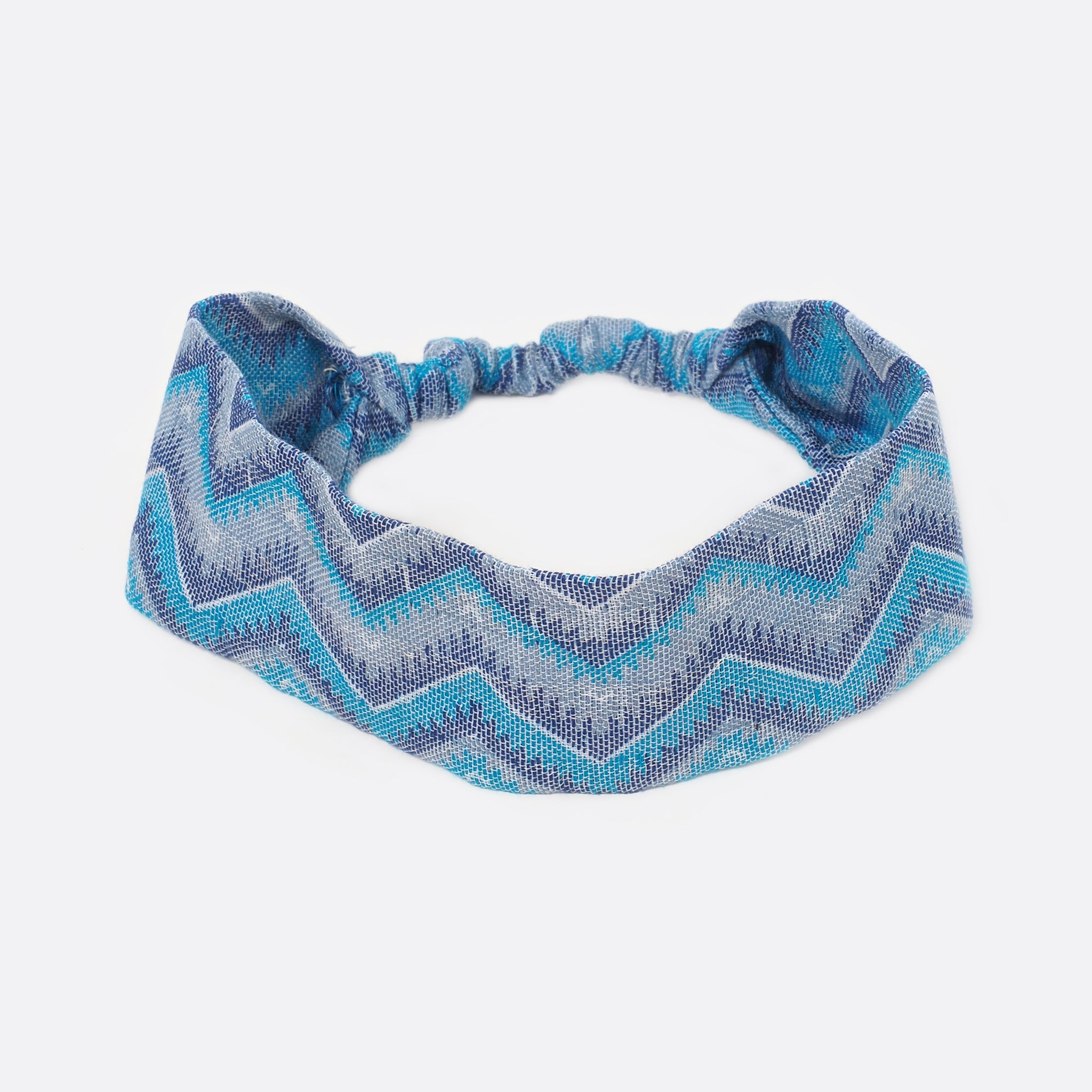 Top view of the Battiayo Sun & Moon Blue headband. The handwoven traditional dhaka fabric has different shades of blue and a bit of white. The dhaka fabric has a geometric pattern and is handwoven by amazing women. The pattern is a zigzag pattern.