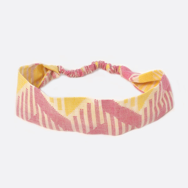 Top view of the Battiayo Pink & Yellow headband. The handwoven traditional dhaka fabric is mainly pink and yellow and a bit white. The dhaka fabric has a geometric pattern and is handwoven by amazing women. The pattern has lines in different length and thickness.