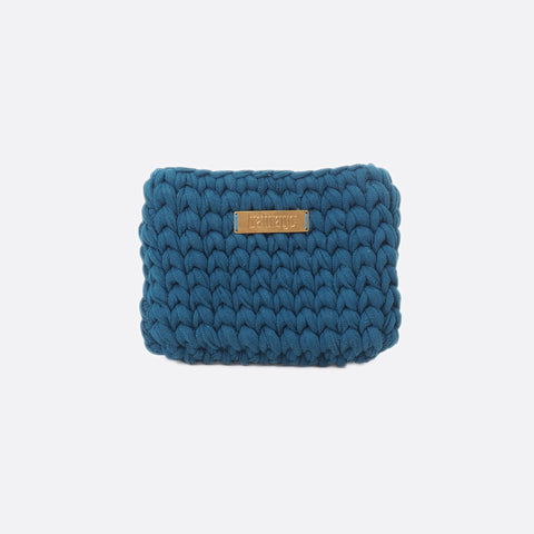 Front view of the small dark blue Battiayo clutch. The bag is crocheted by women. The handcut brass label is placed in the middle of the bag, close to the top. The bag is a chunky crocheted clutch. 
