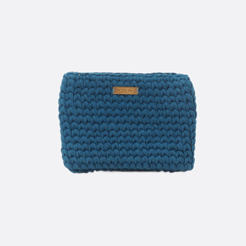 Front view of the medium dark blue Battiayo clutch. The bag is crocheted by women. The handcut brass label is placed in the middle of the bag, close to the top. The bag is a chunky crocheted clutch. 