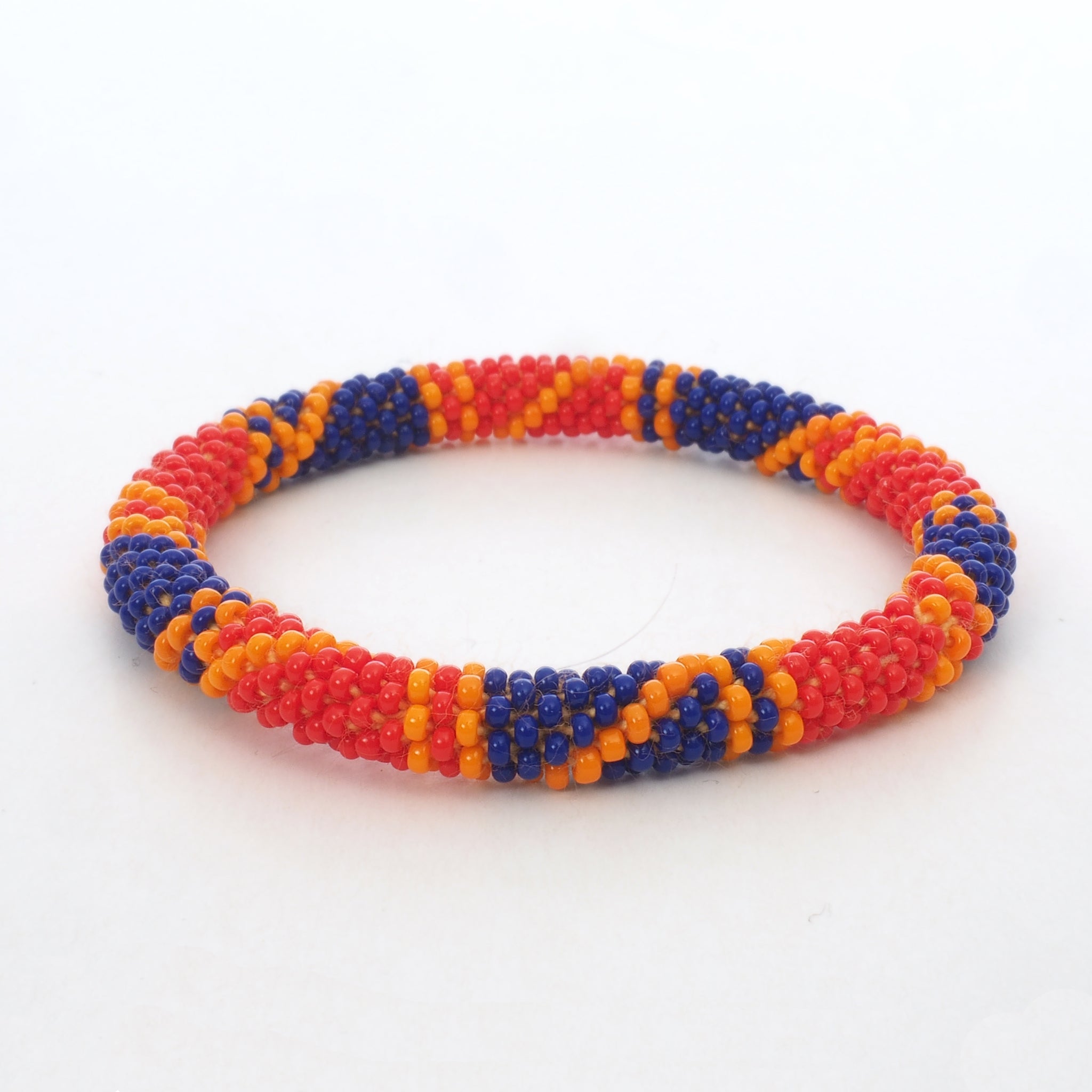 One beaded bracelet is on the picture. The bracelet is made from red, blue and orange glass beads. The bracelet has a geometric pattern. The glass beads are clearly shown. The background of the picture is white.  The Battiayo bracelets are handmade from small glass beads.