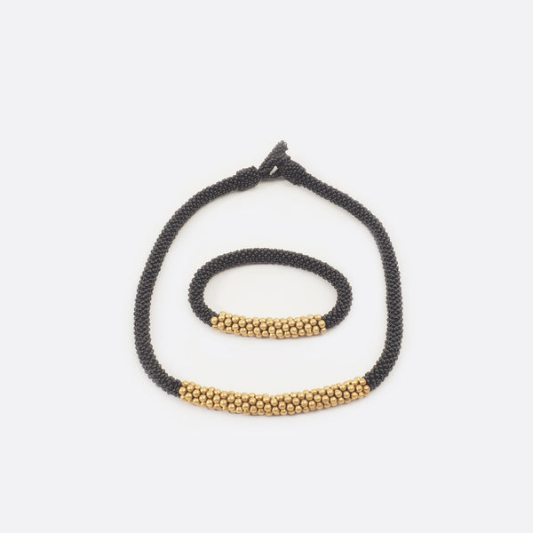 The black beaded single-string necklace with brass is shown with the matching bracelet. The bracelet is mainly black and has in the middle some golden brass beads.