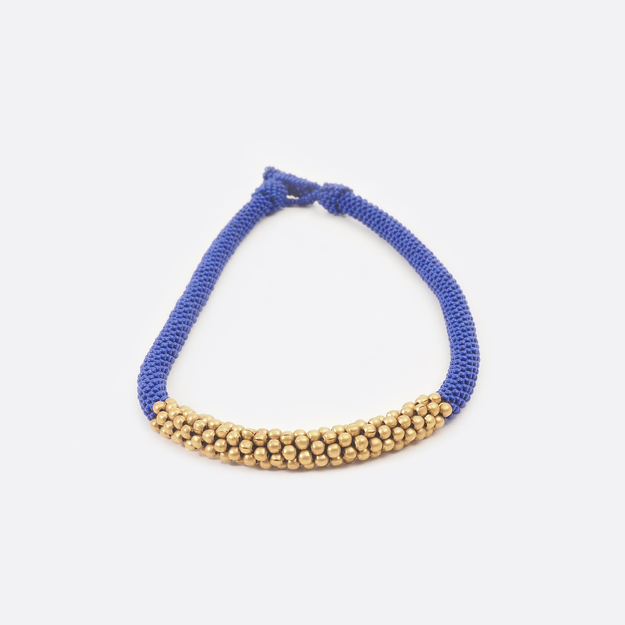 Front view of the handmade Battiayo beaded necklace. It is a single-string necklace. The necklace is mainly blue. The middle part of the necklace is done with golden brass beads. The part of the brass beads is around 7cm long. 