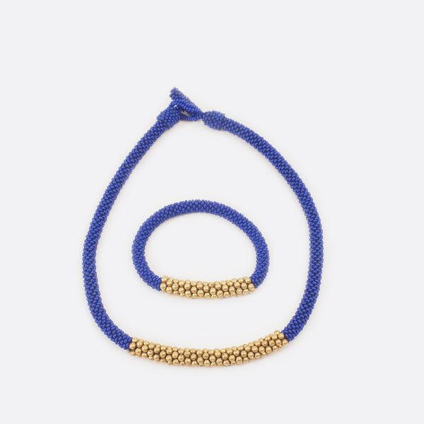 The blue beaded single-string necklace with brass is shown with the matching bracelet. The bracelet is mainly blue and has in the middle some golden brass beads.