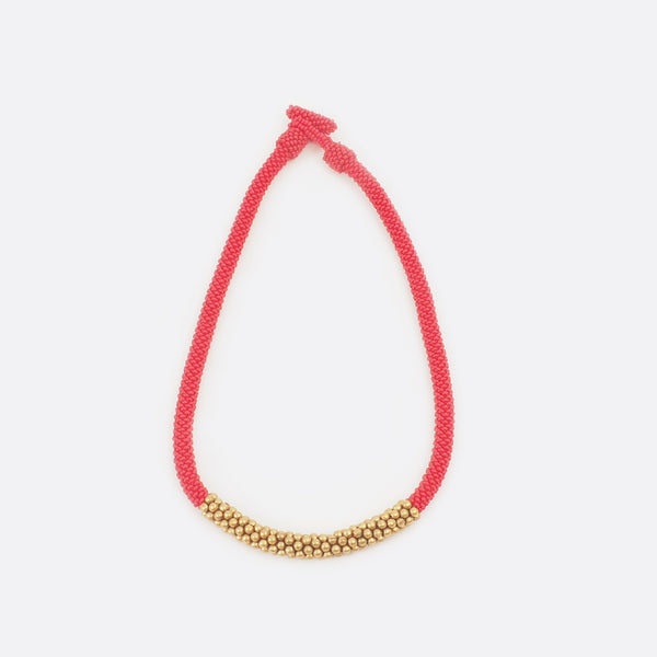 Front view of the handmade Battiayo beaded necklace. It is a single-string necklace. The necklace is mainly red. The middle part of the necklace is done with golden brass beads. The part of the brass beads is around 7cm long. 