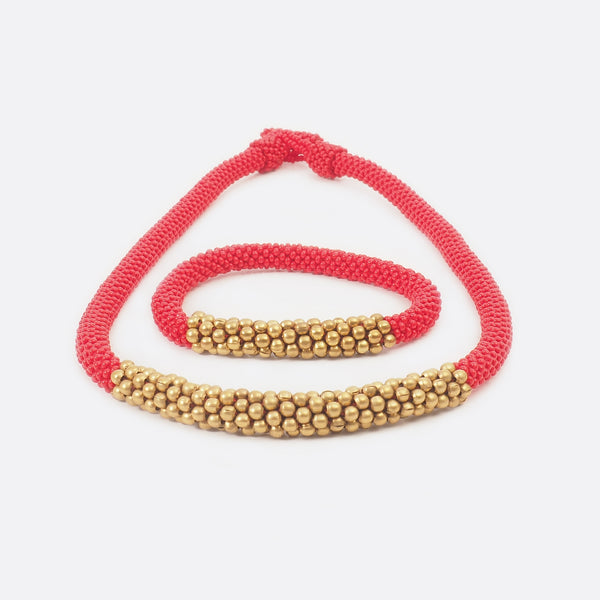 The red beaded single-string necklace with brass is shown with the matching bracelet. The bracelet is mainly red and has in the middle some golden brass beads.