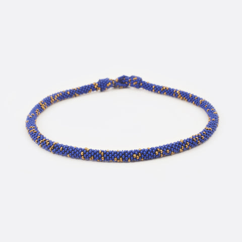 Front view of the handmade Battiayo beaded necklace. It is a single-string necklace. The necklace is mainly blue and has small golden dots.