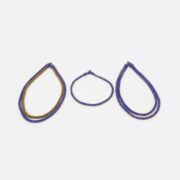 The handmade Battiayo necklace in blue with golden dots is existing in three variations. All three variations are shown on the picture. On the left is the double-string necklace with both strings in blue with golden dots. In the middle is the single-string necklace, which is much shorter than the double-string necklace. On the right is the double-string necklace with the longer string in blue with golden dots and the shorter string completely golden.