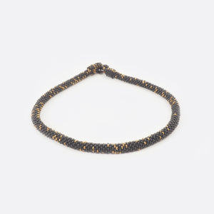 Front view of the handmade Battiayo beaded necklace. It is a single-string necklace. The necklace is mainly black and has small golden dots.