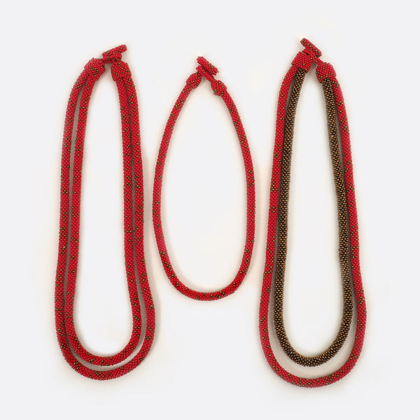 The handmade Battiayo necklace in red with golden dots is existing in three variations. All three variations are shown on the picture. On the left is the double-string necklace with both strings in red with golden dots. In the middle is the single-string necklace, which is much shorter than the double-string necklace. On the right is the double-string necklace with the longer string in red with golden dots and the shorter string completely golden.