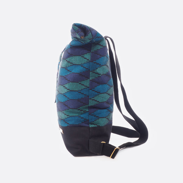Side view of the Battiayo ,Deep Blue Sea’ backpack with handwoven dhaka fabric. The backpack is closed with a zipper and as well with a buckle. The upper part of the backpack has the dhaka fabric and the bottom part is made from black canvas fabric.