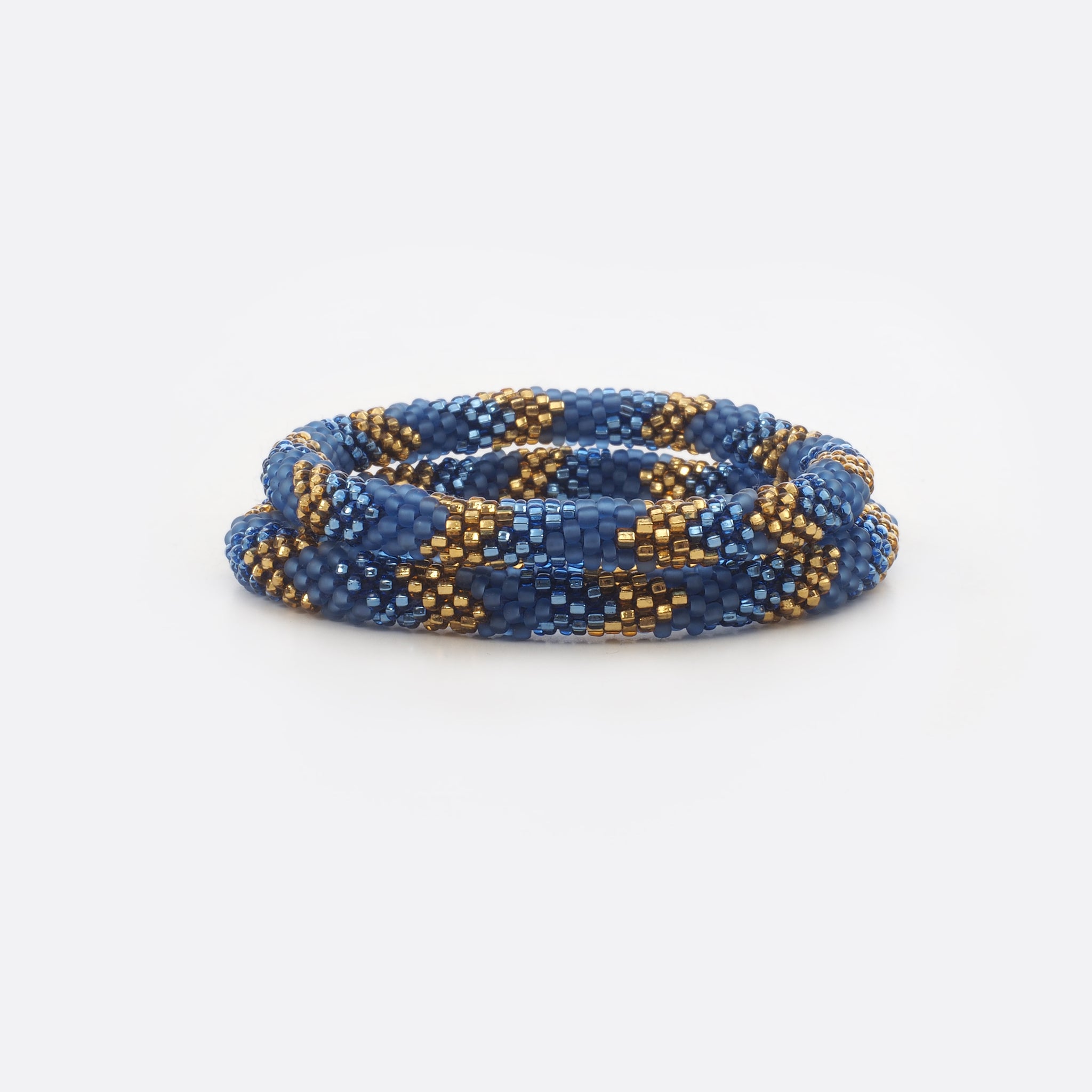 Set of two beaded bracelets.  The bracelets are made from mat blue, shiny blue and shiny golden glass beads. The bracelets have the same geometric pattern. The Battiayo bracelets are handmade from small glass beads. The glass beads are clearly shown. The background of the picture is white.