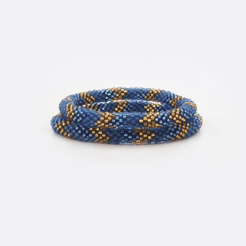 Set of two beaded bracelets.  The bracelets are made from mat blue, shiny blue and shiny golden glass beads. The bracelets have the same geometric pattern. The Battiayo bracelets are handmade from small glass beads. The glass beads are clearly shown. The background of the picture is white.