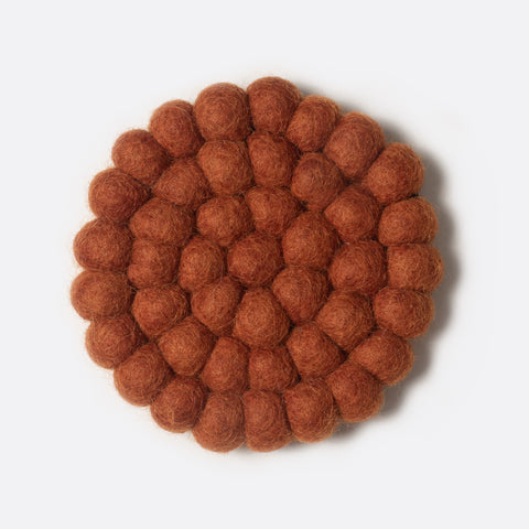 Round small felt coaster which is made from little felt balls. The color is red orange.