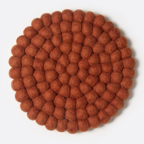 Round felt coaster which is made from little felt balls. The color is red orange.