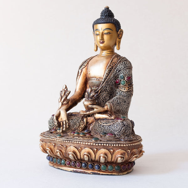 Bhaisajyaguru Statue made of copper, lost wax casting, silver and gold plated, set with filigree and set synthetic gemstones in ruby red, emerald green, lapis lazuli blue. The face is set in gold. Handmade in Nepal