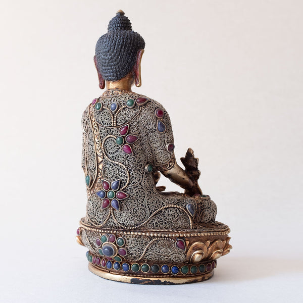 Bhaisajyaguru Statue made of copper, lost wax casting, silver and gold plated, set with filigree and set synthetic gemstones in ruby red, emerald green, lapis lazuli blue. The face is set in gold. Handmade in Nepal